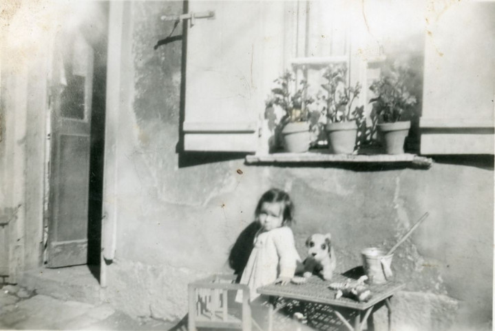 Maryvonne Thoréton avec son petit banc, la petite table en osier, seau de plage et son petit chien en tissu, sous la fenêtre de la rue Candie : photographie noir et blanc, DR, 6 x 8.8, (septembre 1950),(collection particulière Maryvonne Thoréton, AMA, 2018.)